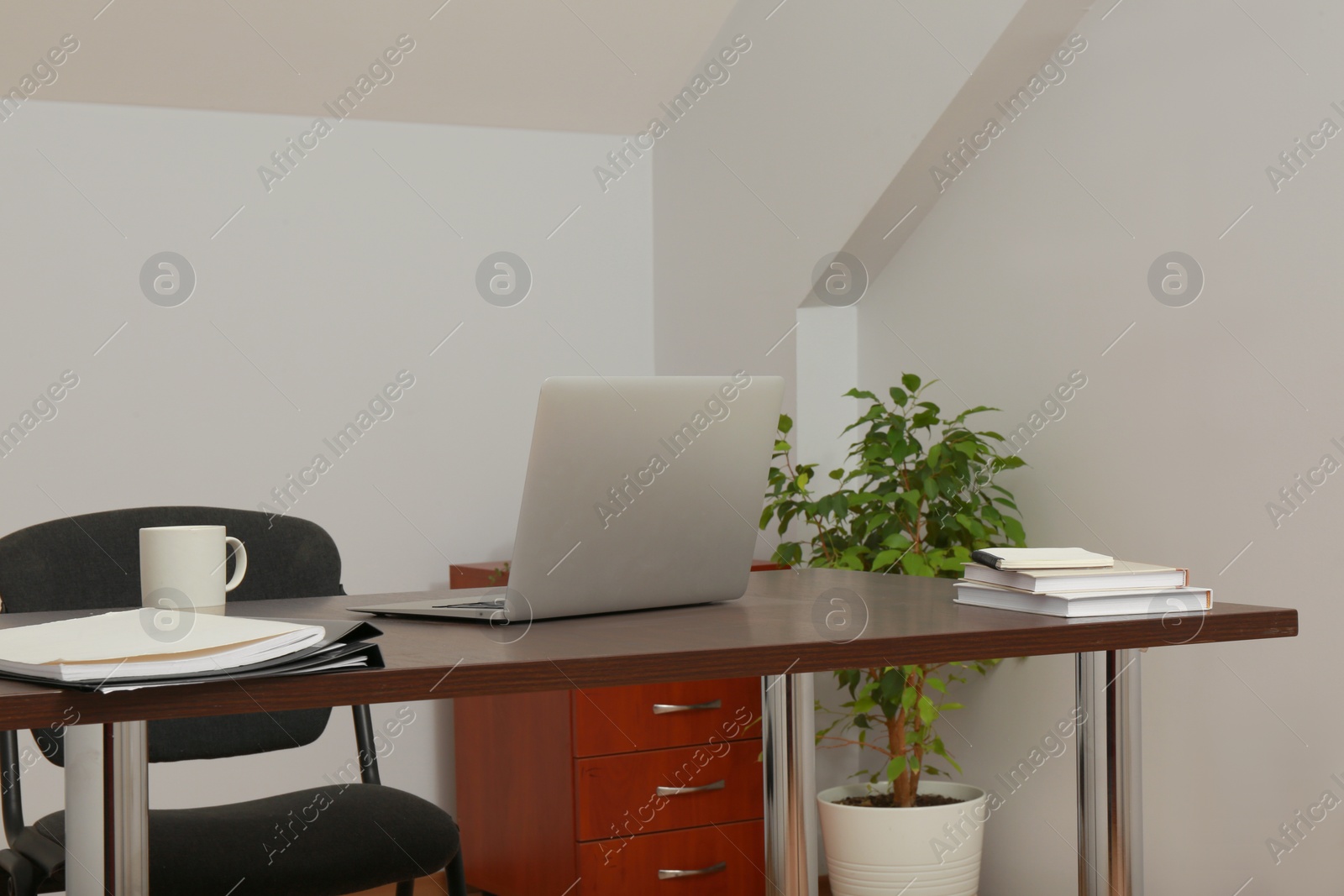 Photo of Stylish workplace with laptop and documents in attic room. Interior design