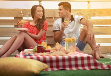 Happy couple with tasty snacks imitating picnic at home