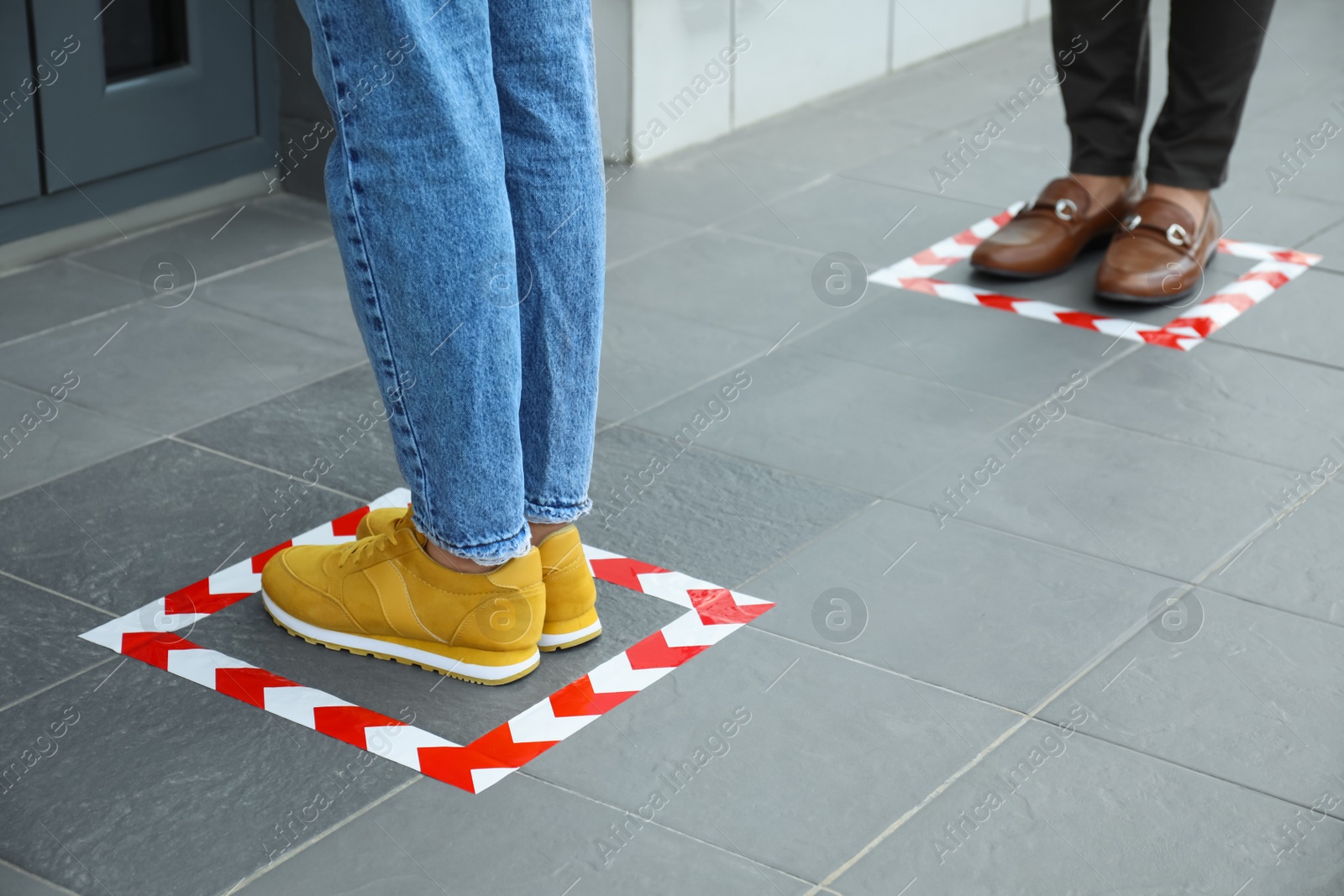 Photo of People standing on taped floor markings for social distance, closeup. Coronavirus pandemic
