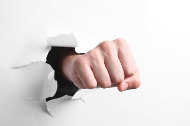 Photo of Man breaking through white paper with fist, closeup
