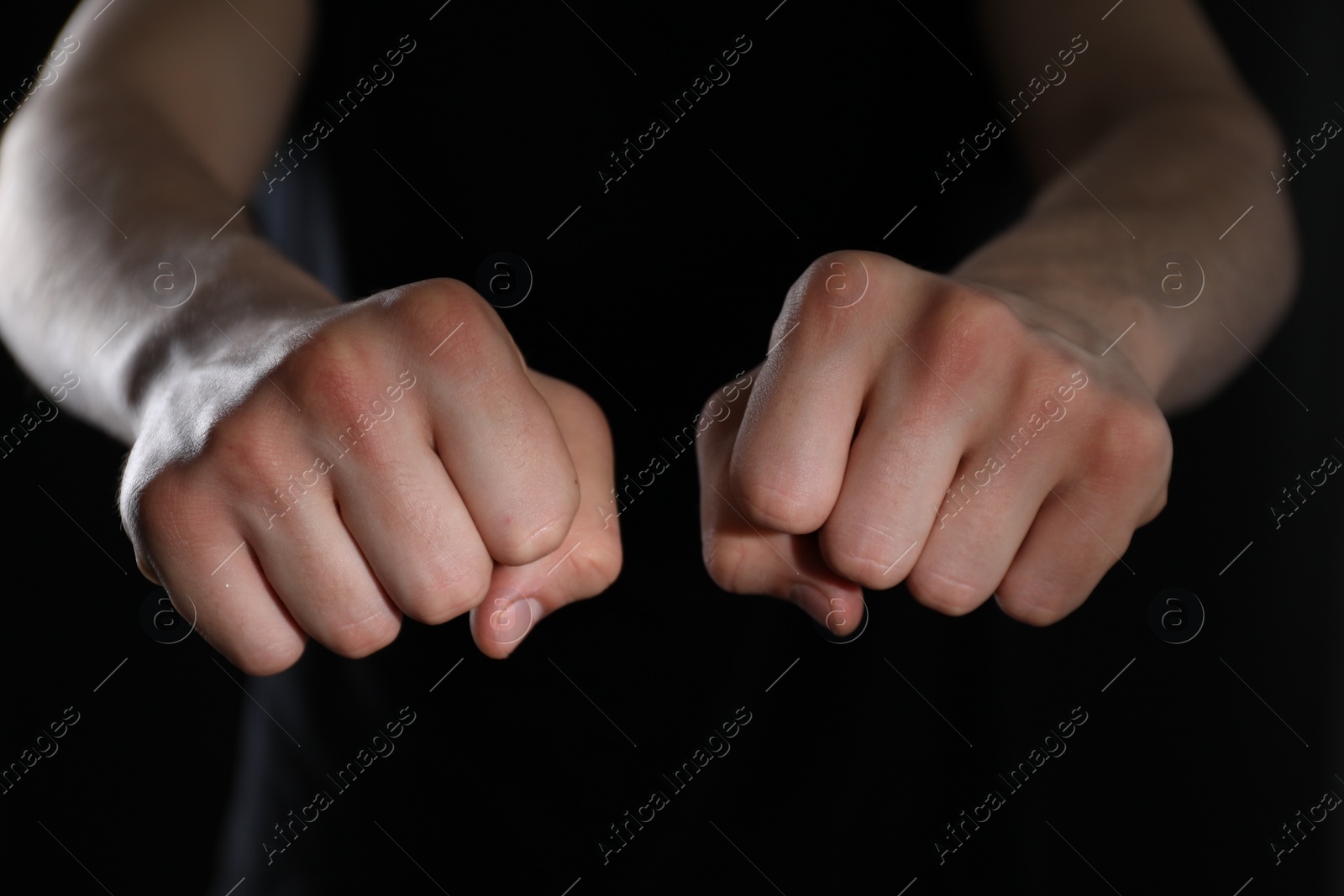 Photo of Man showing fists with space for tattoo on black background, closeup