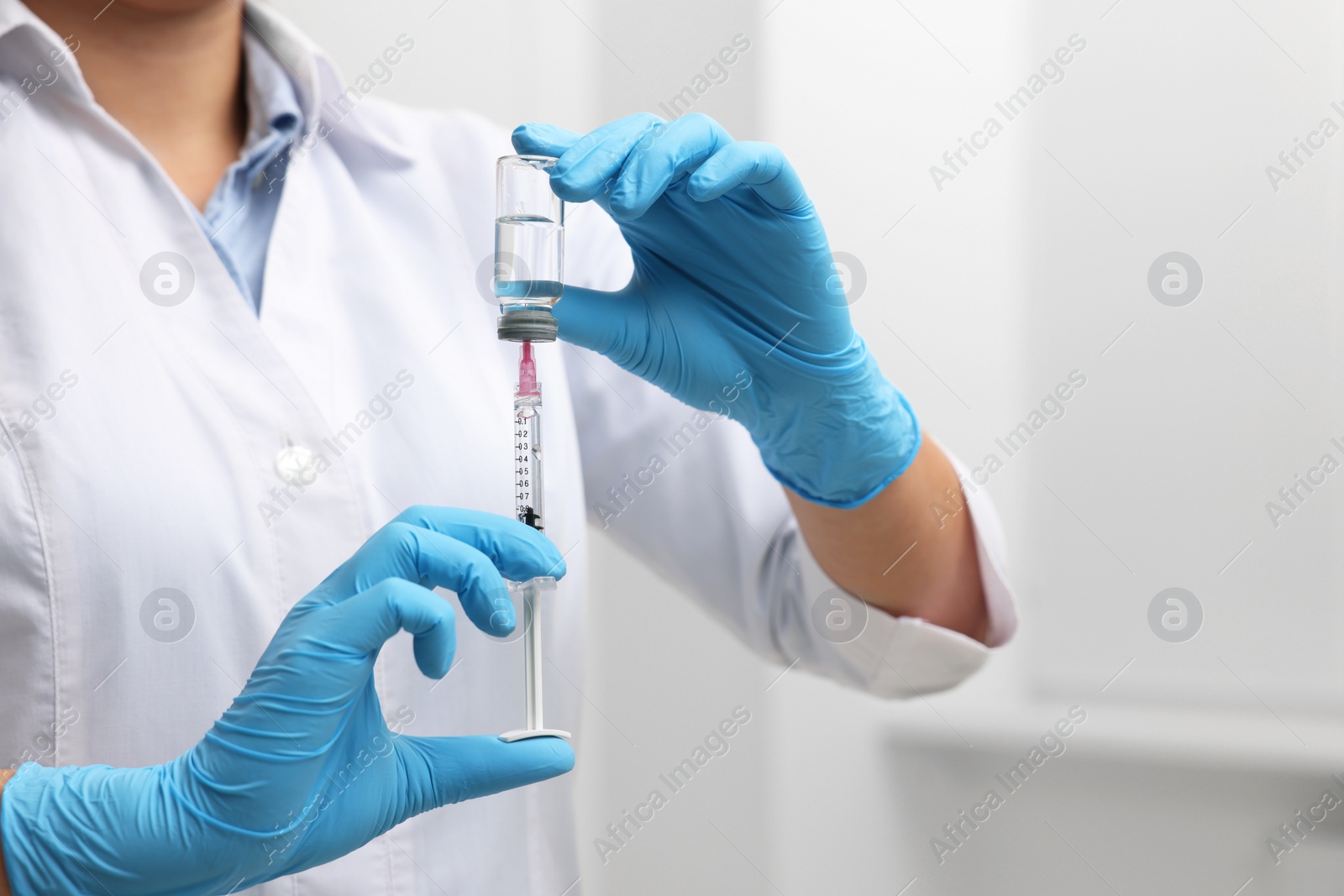 Photo of Doctor filling syringe with medication from glass vial indoors, closeup. Space for text