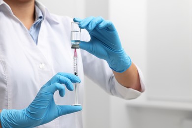 Doctor filling syringe with medication from glass vial indoors, closeup. Space for text