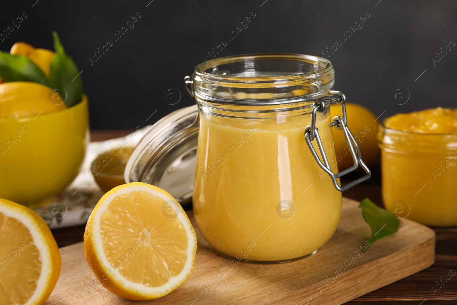 Photo of Delicious lemon curd in glass jars, fresh citrus fruits and green leaves on wooden table