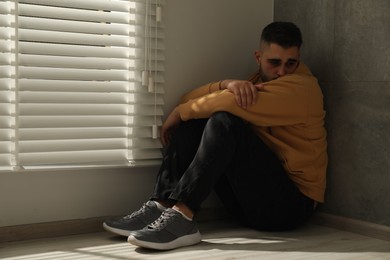 Photo of Sad man sitting on floor near window. Space for text