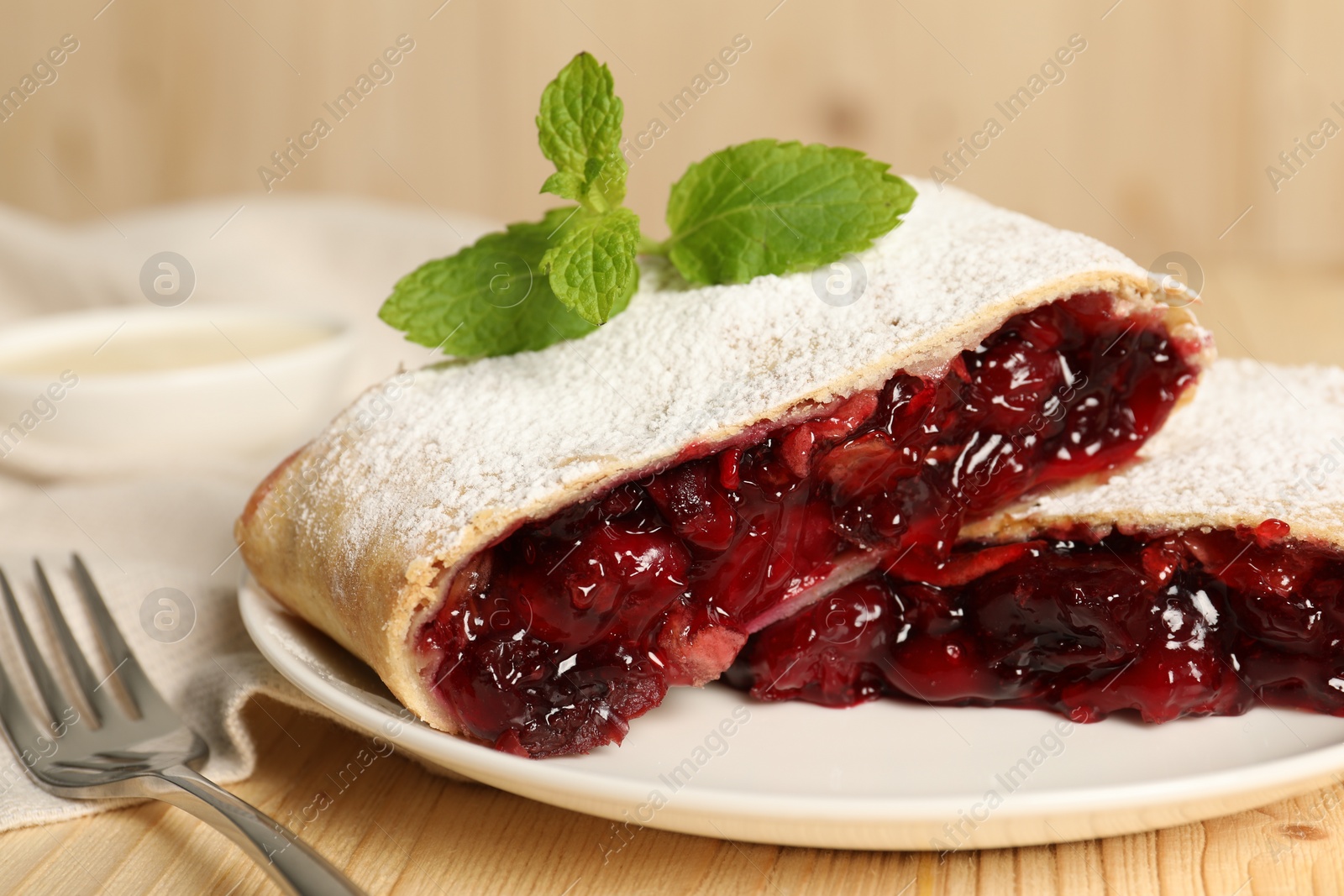 Photo of Delicious strudel with cherries, powdered sugar and mint on wooden table, closeup