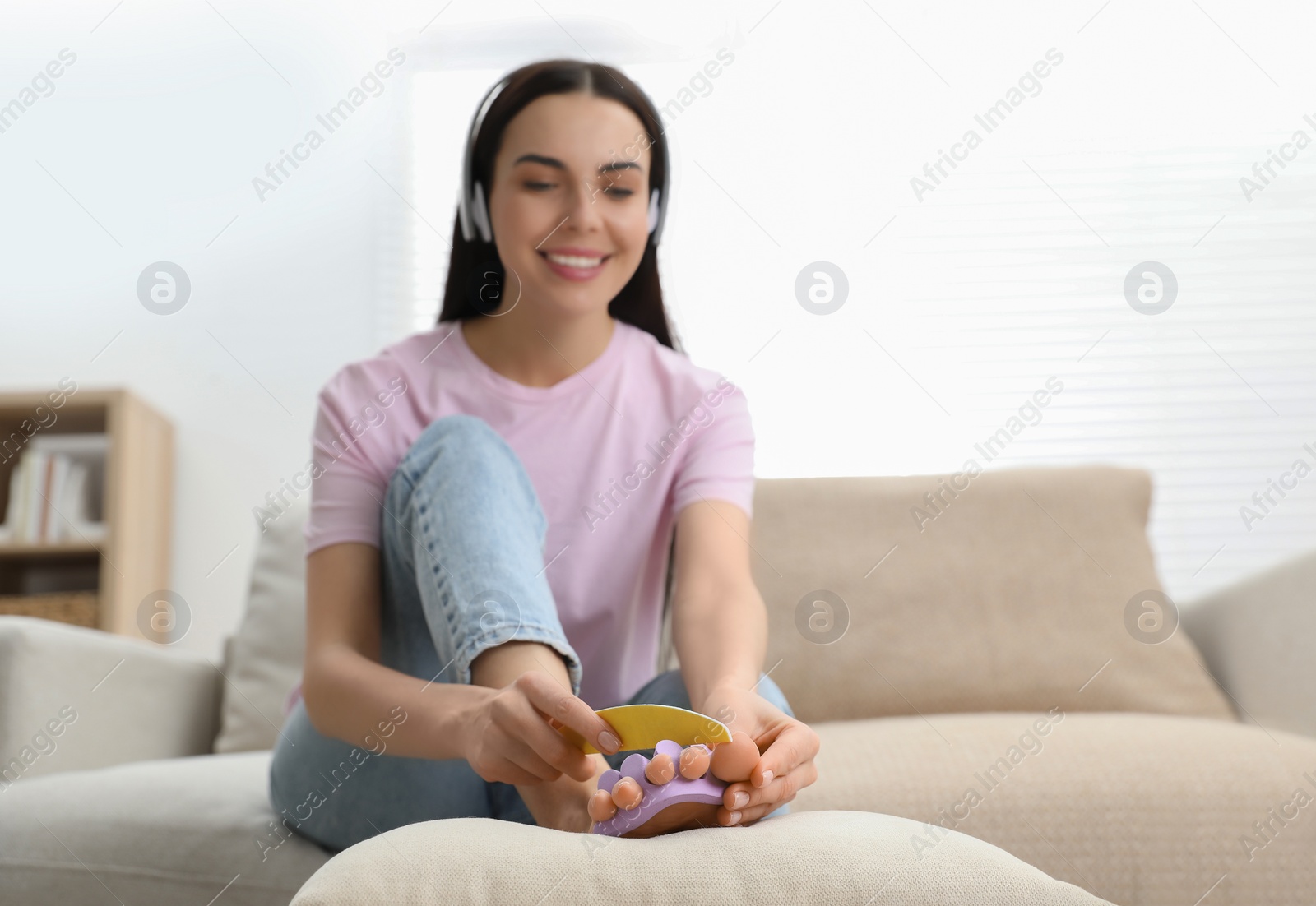 Photo of Beautiful young woman listening to music while giving herself pedicure in living room, selective focus