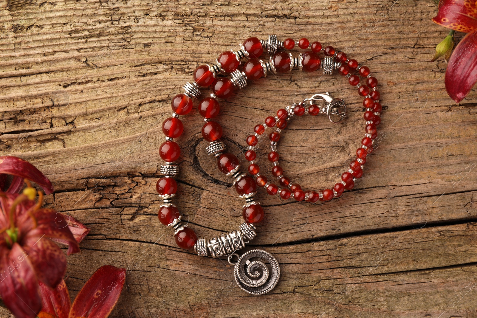 Photo of Beautiful necklace with gemstones and lily flowers on wooden surface, flat lay