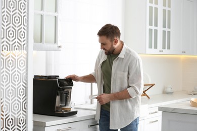 Photo of Young man preparing fresh aromatic coffee with modern machine in kitchen