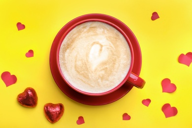 Cup of coffee, chocolate candies and paper hearts on yellow background, flat lay. Valentine's day breakfast
