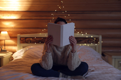 Photo of Young woman reading book on bed at home