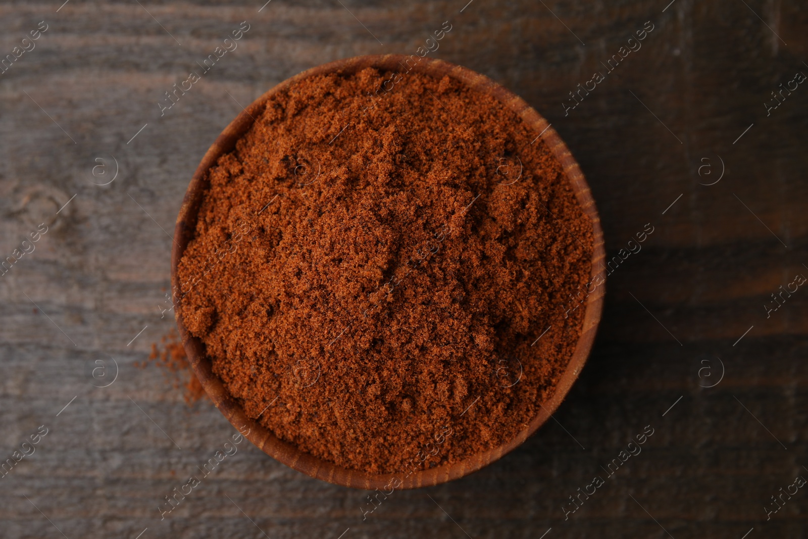 Photo of Nutmeg powder in bowl on wooden table, top view