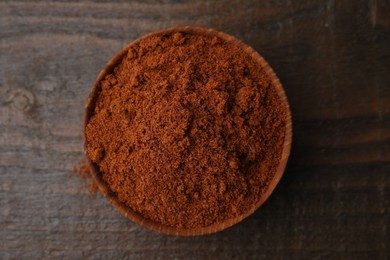 Nutmeg powder in bowl on wooden table, top view