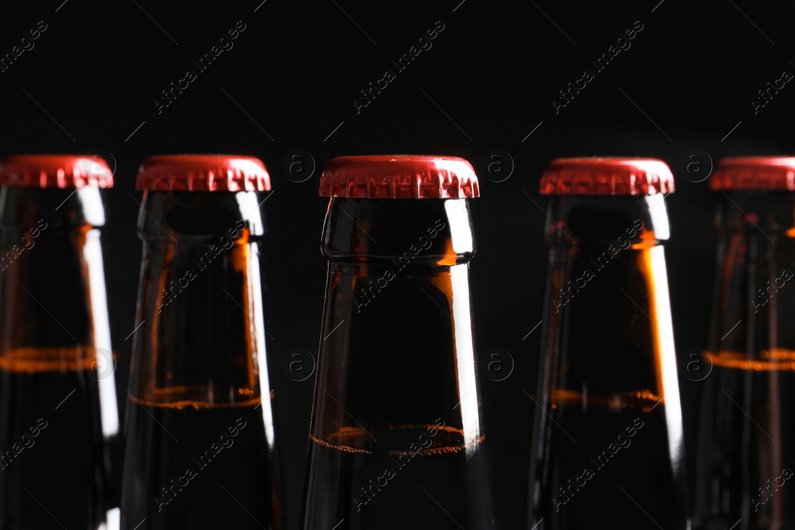 Photo of Bottles of tasty cold beer on black background, closeup