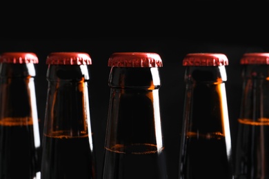 Photo of Bottles of tasty cold beer on black background, closeup