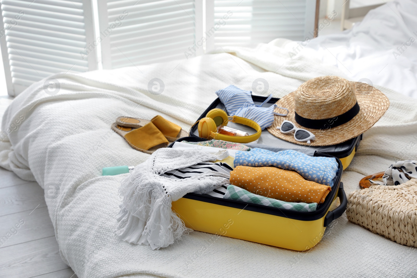 Photo of Open suitcase full of clothes, shoes and summer accessories on bed