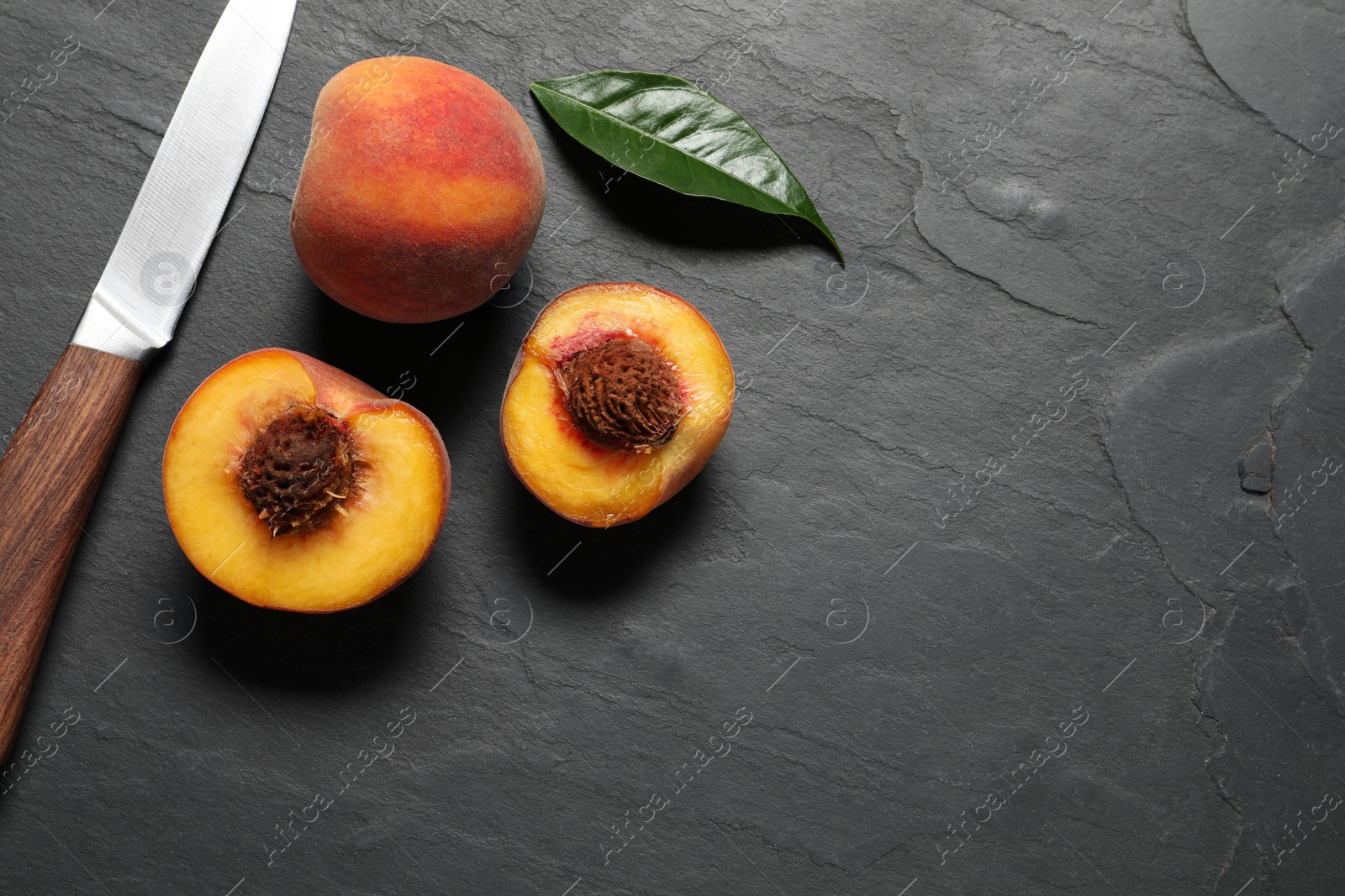 Photo of Delicious juicy peaches, leaf and knife on black textured table, flat lay. Space for text