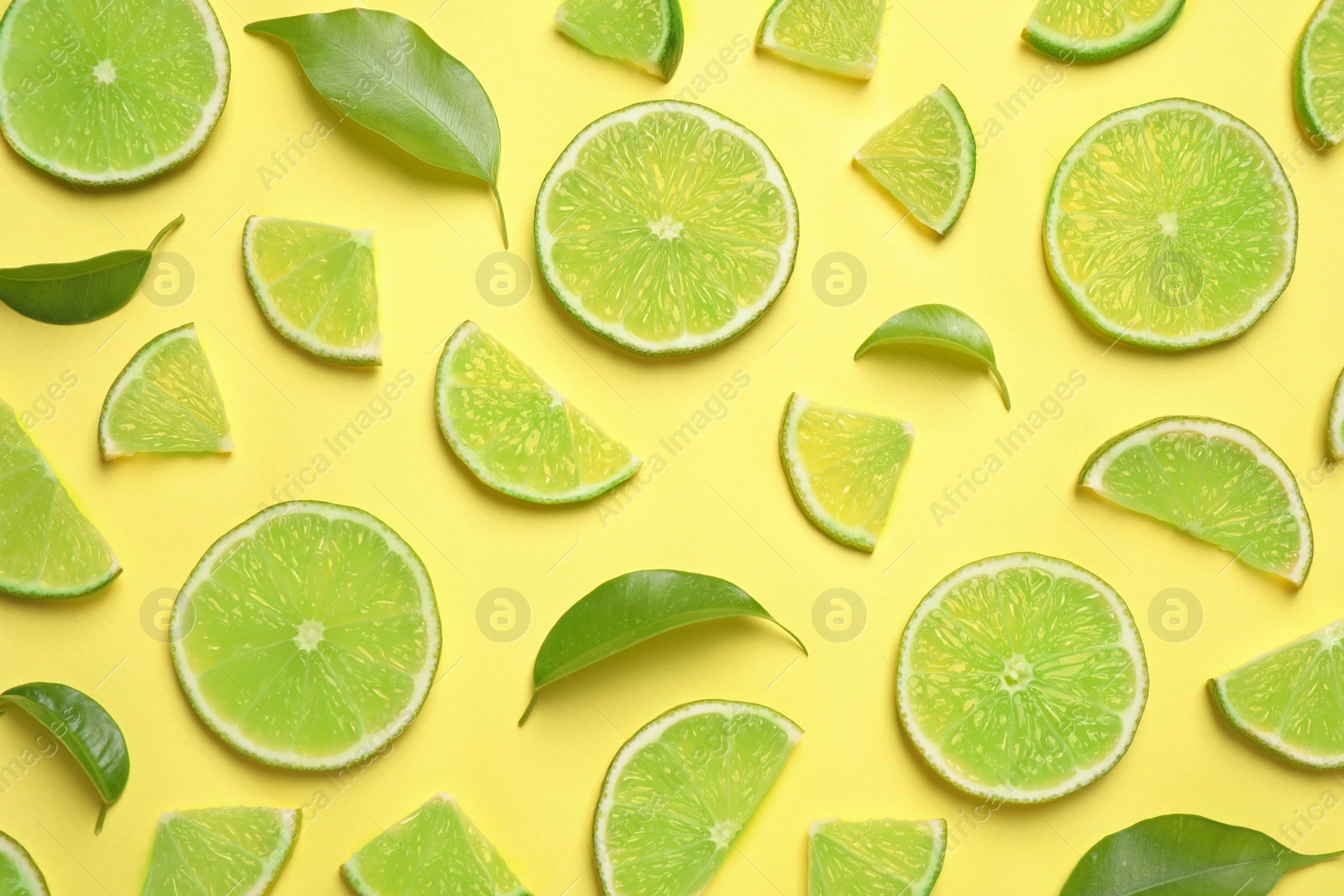 Photo of Juicy fresh lime slices and green leaves on yellow background, flat lay