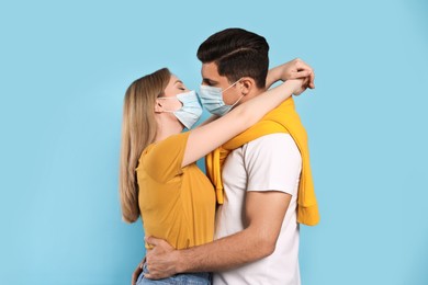 Couple in medical masks trying to kiss on light blue background