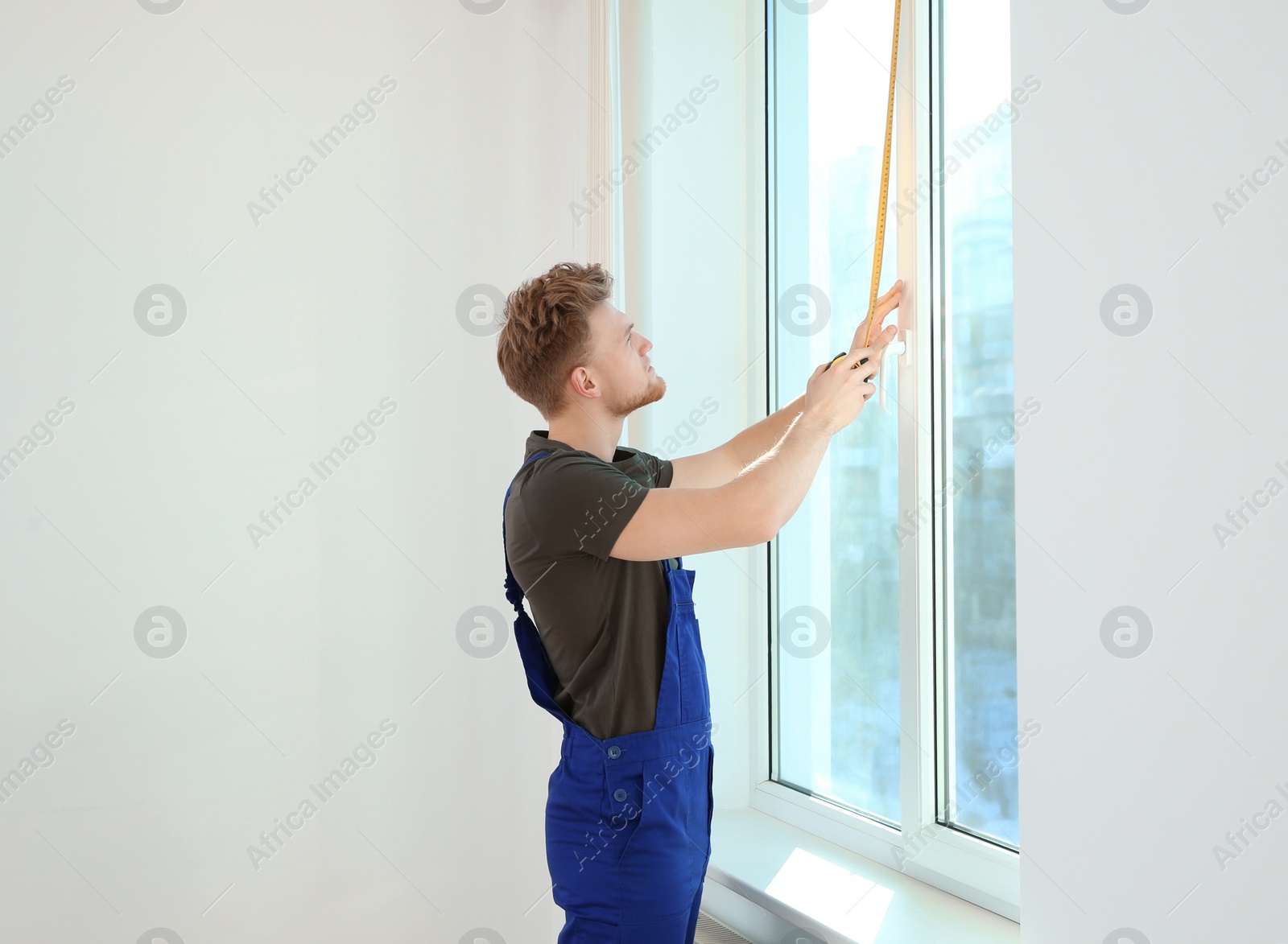 Photo of Service man measuring window for installation indoors. Space for text