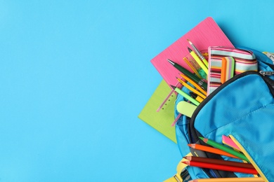 Photo of Backpack with different stationery on light blue background, top view and space for text. Back to school