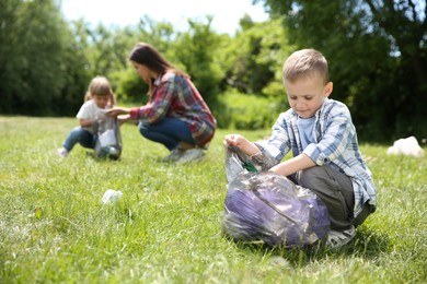 Mother and her children with plastic bags collecting garbage in park