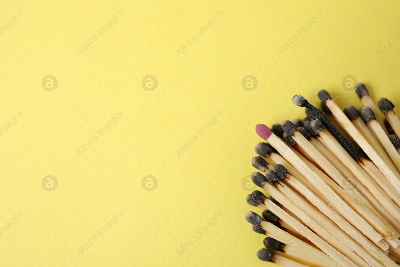 Photo of Heap of burnt matches and whole one on yellow background, flat lay. Space for text