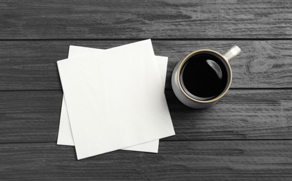 Cup of coffee and clean paper napkins on wooden background, top view