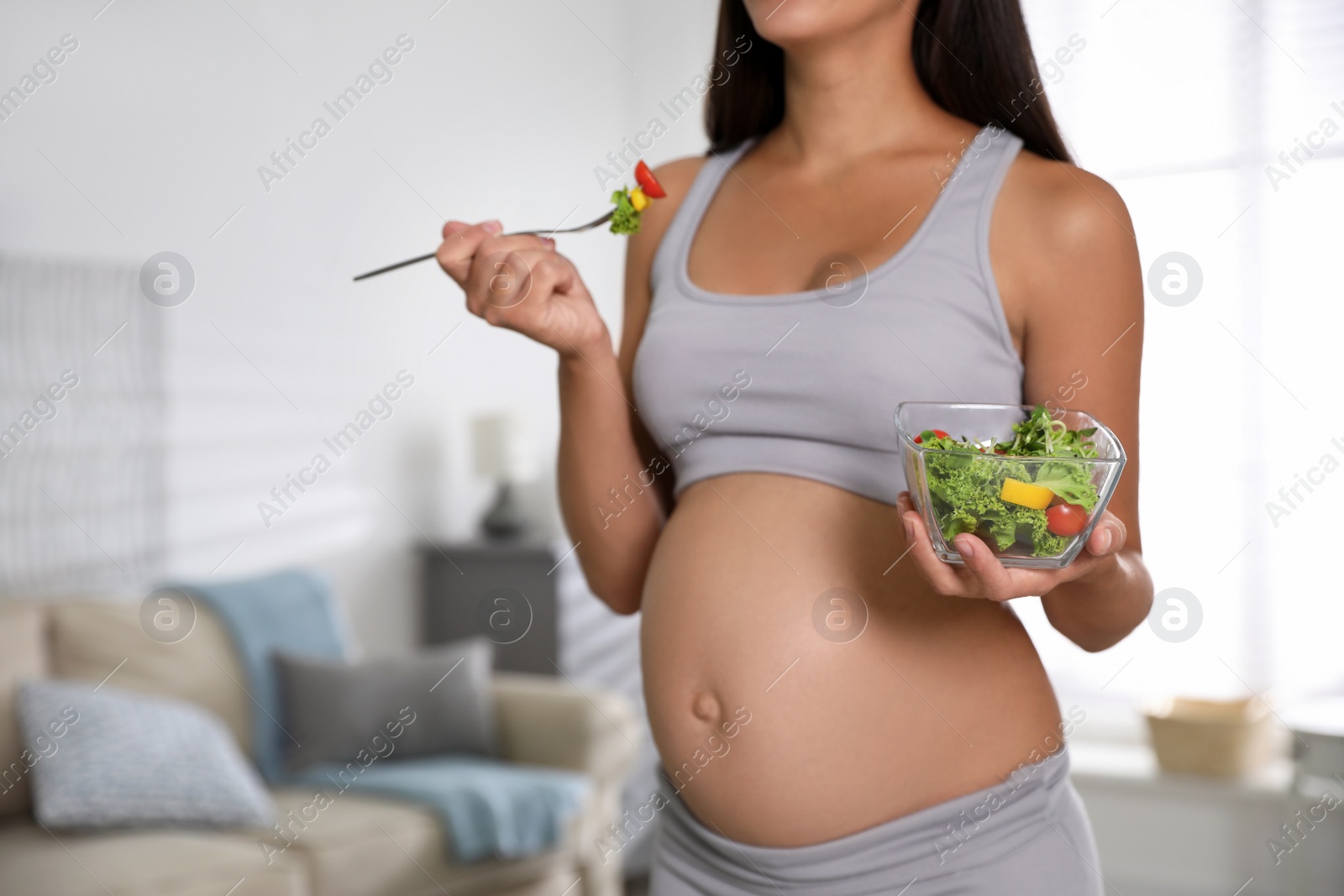 Photo of Young pregnant woman with bowl of vegetable salad in living room, closeup. Taking care of baby health
