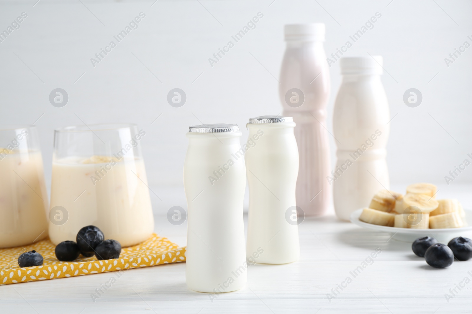 Photo of Tasty yogurt in bottles, banana and blueberries on white wooden table