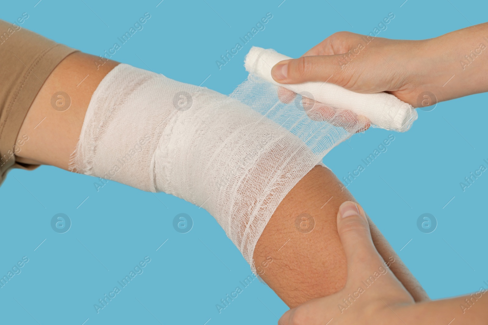 Photo of Doctor applying bandage onto patient's arm on light blue background, closeup