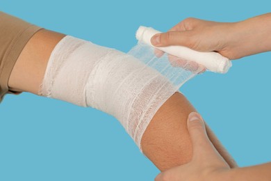 Doctor applying bandage onto patient's arm on light blue background, closeup