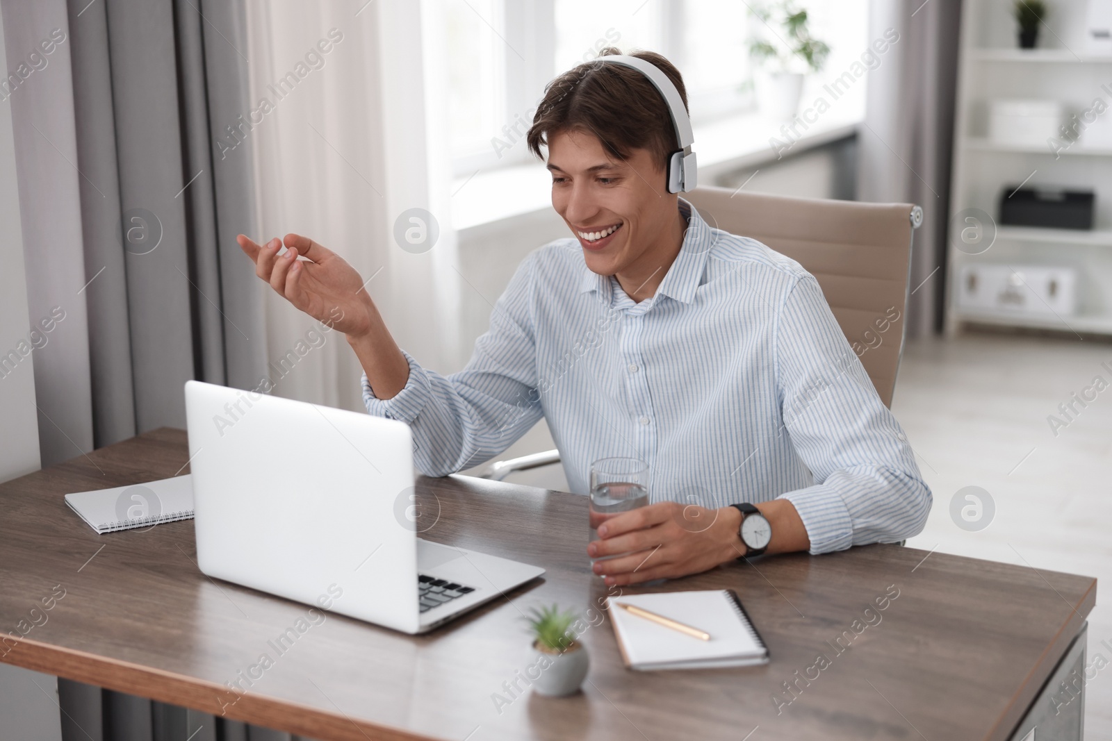 Photo of Man in headphones using video chat during webinar at wooden table in office