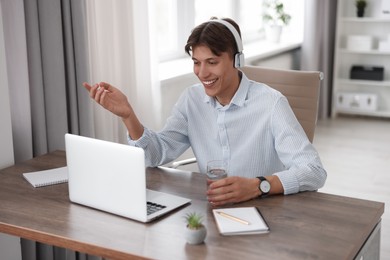 Man in headphones using video chat during webinar at wooden table in office