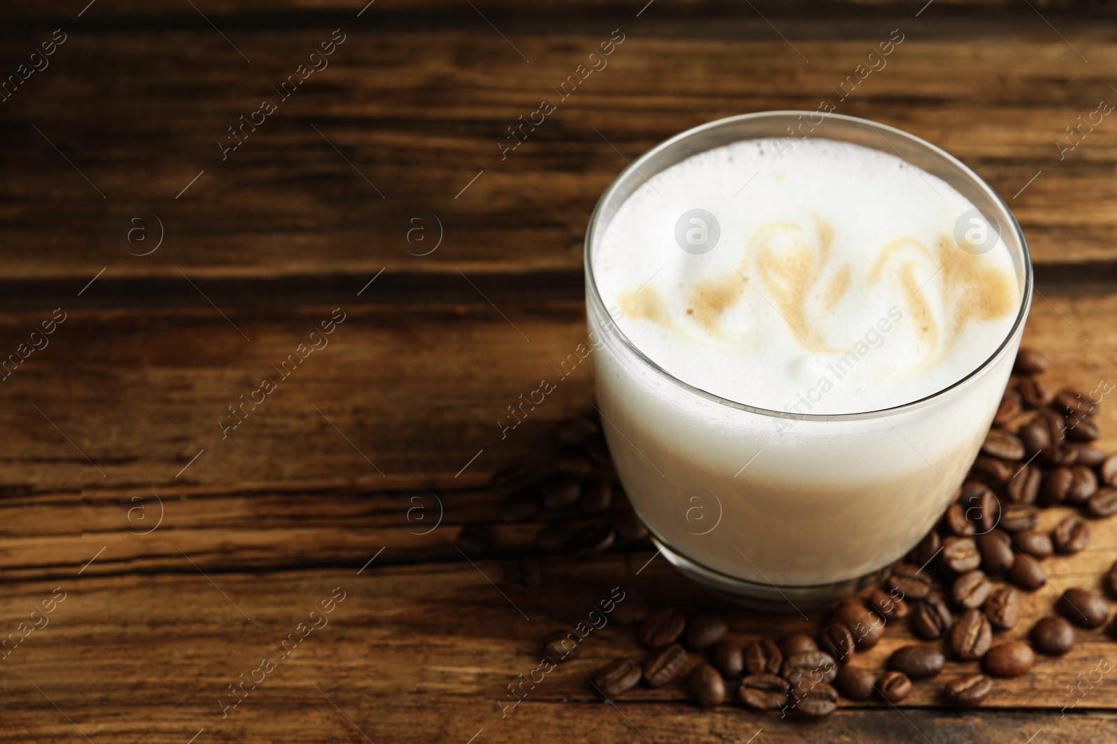 Photo of Delicious latte macchiato and coffee beans on wooden table, space for text