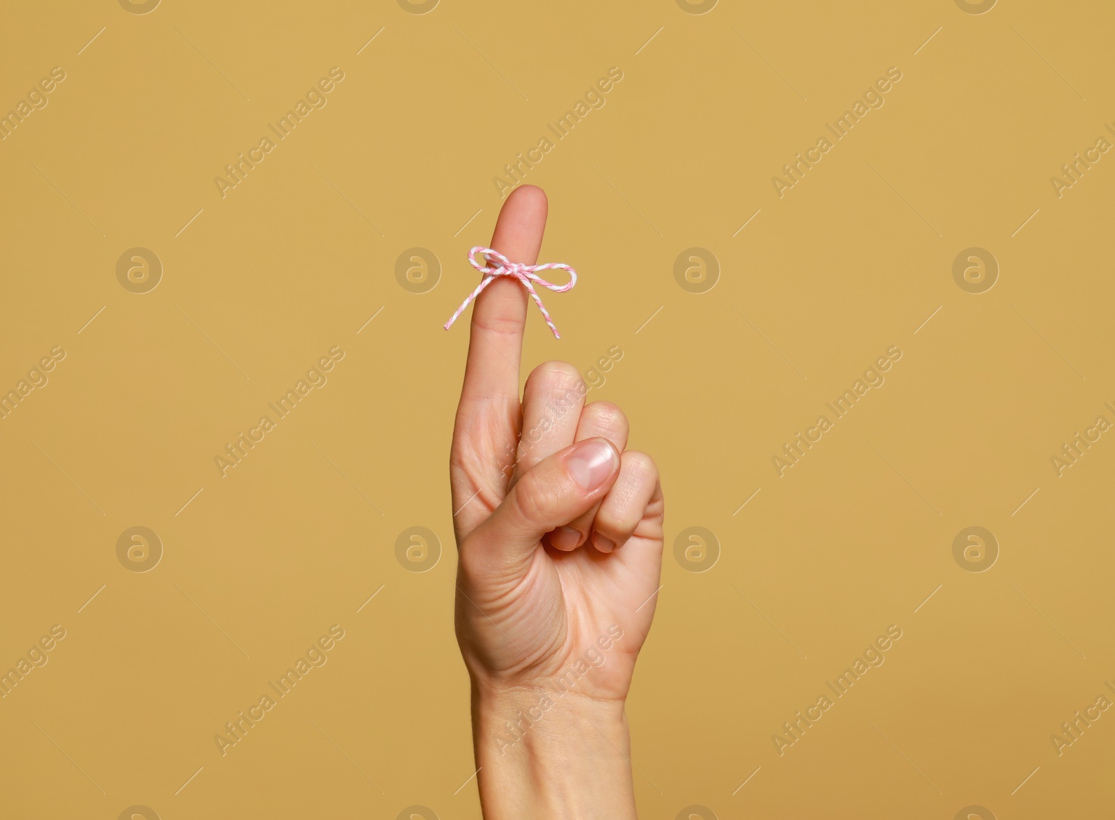 Photo of Woman showing index finger with tied bow as reminder on light brown background, closeup. Space for text