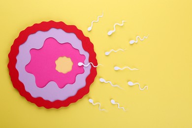 Photo of Fertilization concept. Sperm cells swimming towards egg cell on yellow background, top view