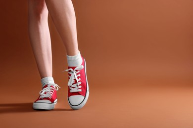 Photo of Woman wearing red classic old school sneakers on brown background, closeup. Space for text