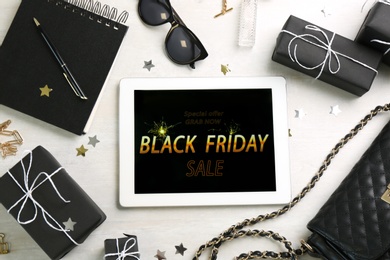 Photo of Flat lay composition with tablet, gifts and accessories on white table. Black Friday sale