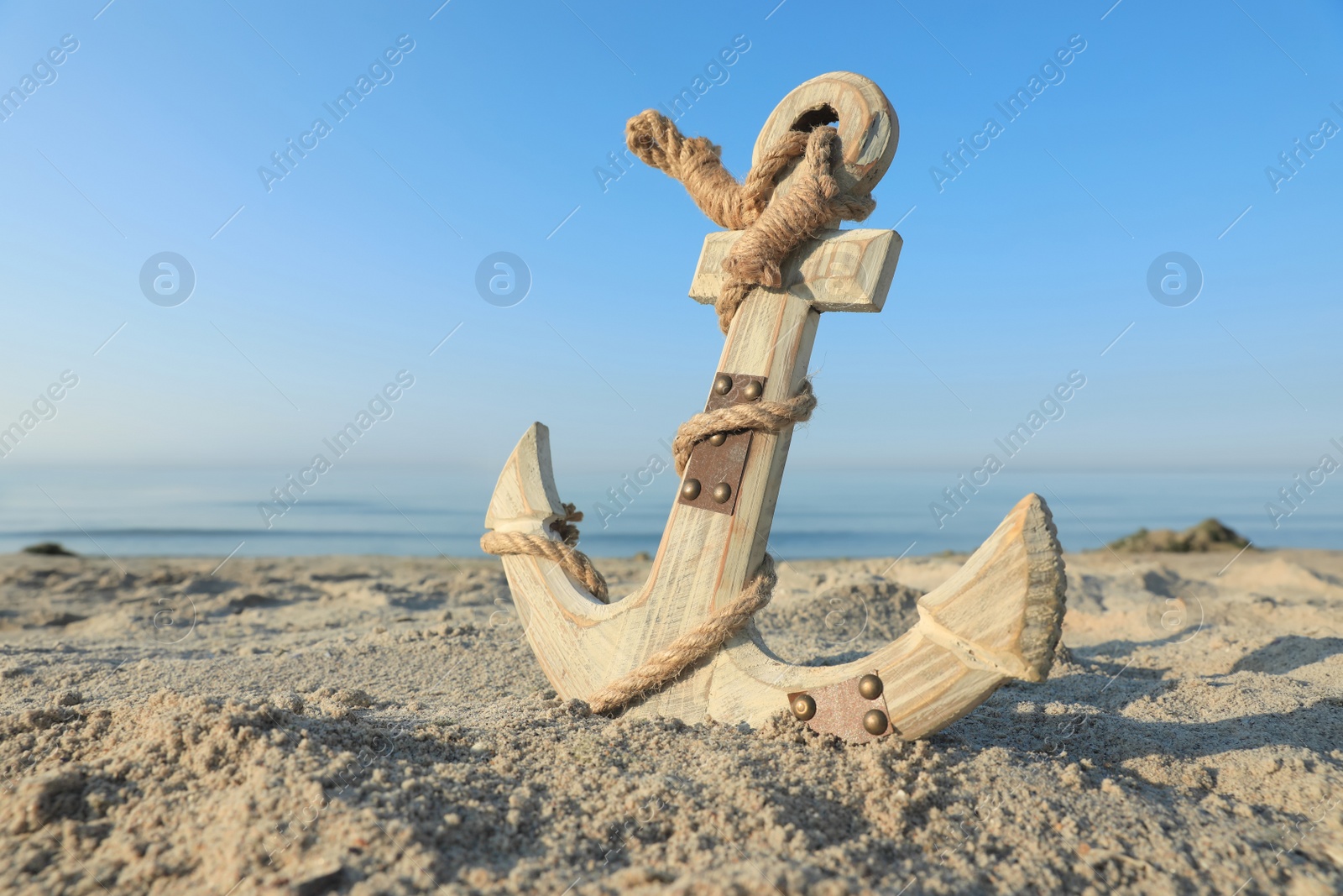 Photo of Wooden anchor with rope on sand near sea. Space for text