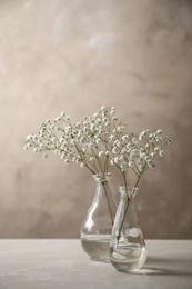 Photo of Gypsophila flowers in vases on table against brown background