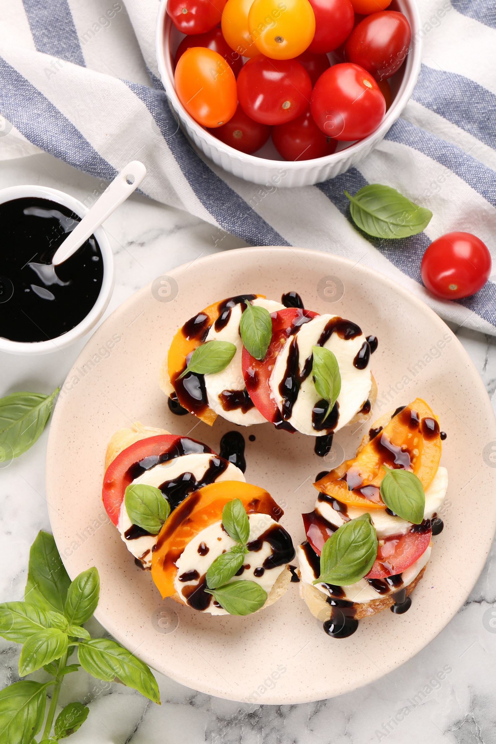 Photo of Delicious bruschettas with mozzarella cheese, tomatoes, balsamic vinegar and ingredients on white table, flat lay