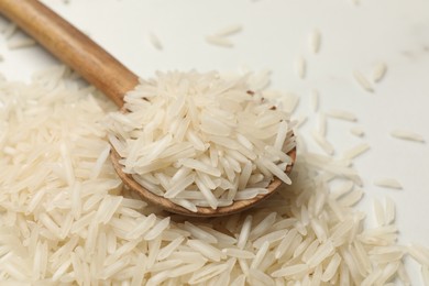 Photo of Raw basmati rice with spoon on white table, closeup