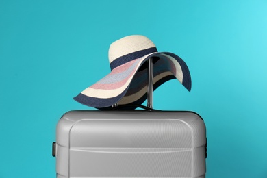 Stylish suitcase with hat on color background