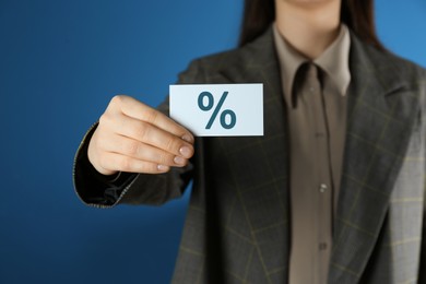 Woman showing business card with percent sign on blue background, closeup. Discount concept