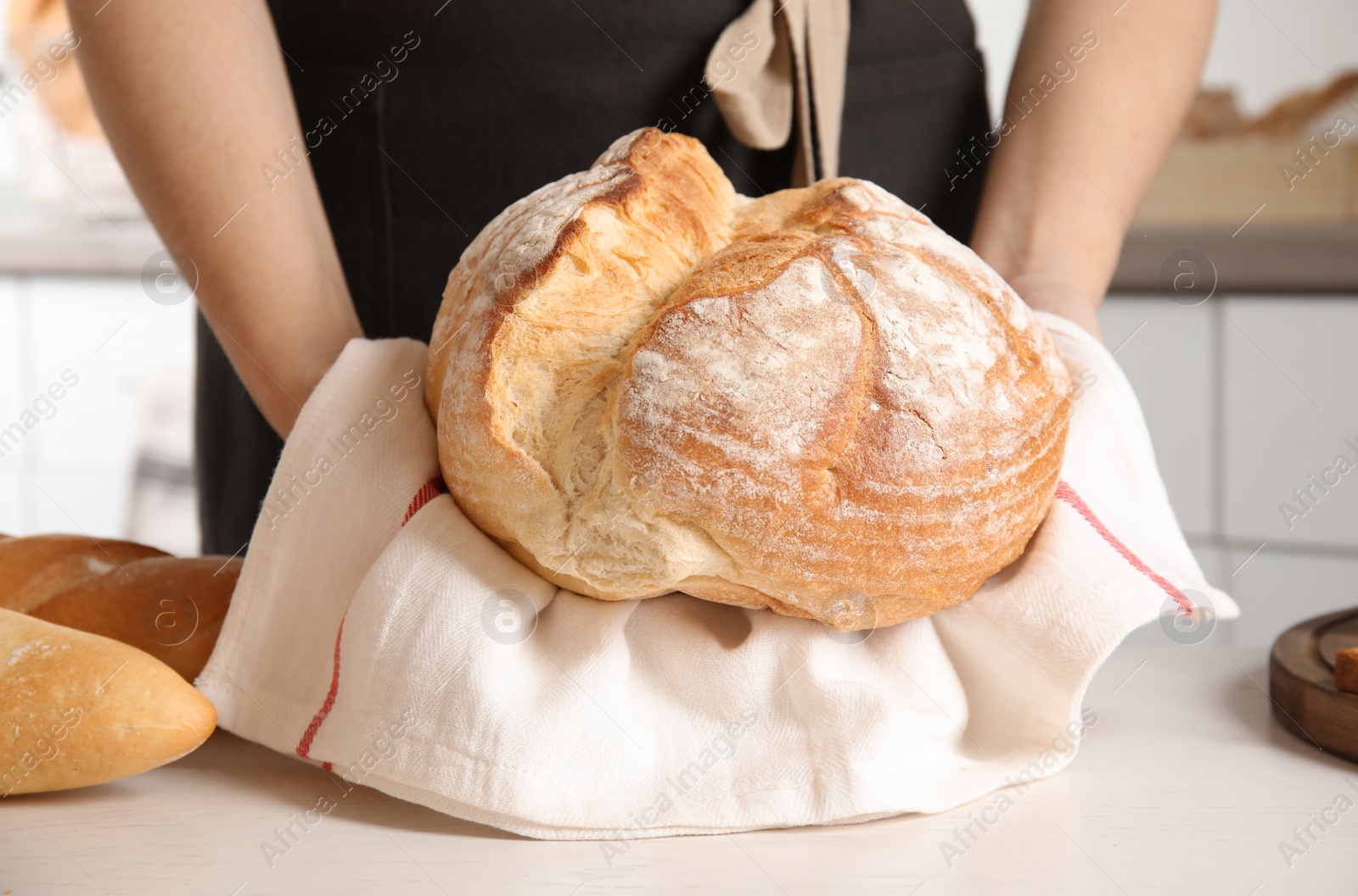 Photo of Baker with loaf of bread at table indoors, closeup