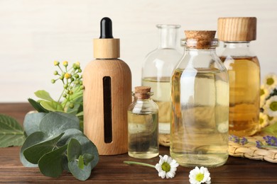 Photo of Aromatherapy. Different essential oils, eucalyptus leaves and flowers on wooden table