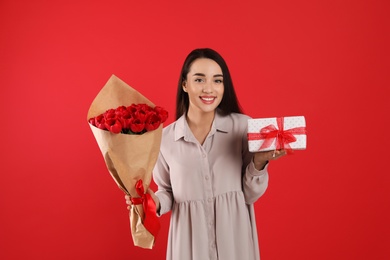 Photo of Happy woman with tulip bouquet and gift box on red background. 8th of March celebration