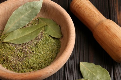 Photo of Mortar, pestle with whole and ground aromatic bay leaves in wooden bowl, closeup