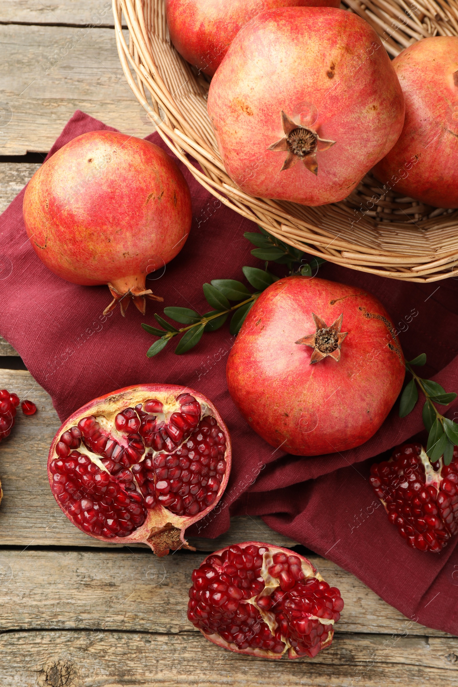 Photo of Fresh pomegranates and green leaves on wooden table, top view